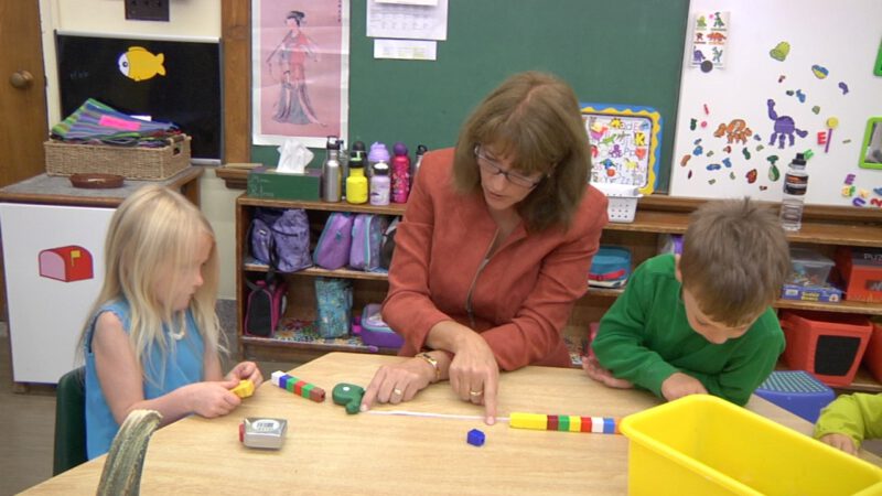 Teacher guides young students in FSL activity with colorful blocks on a table.