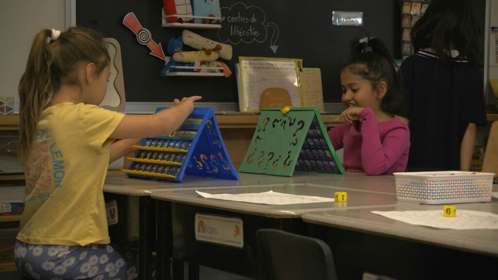 Two girls are seated at a desk across from each other in a classroom and are playing a memory game.