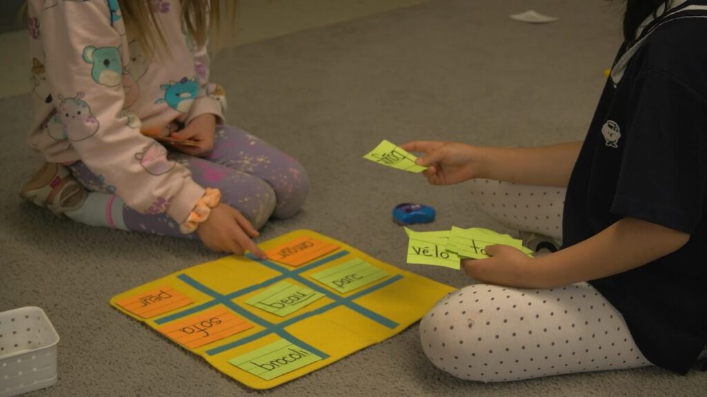Two kids are seated on the floor with a 3x3 grid  with flashcards between them.